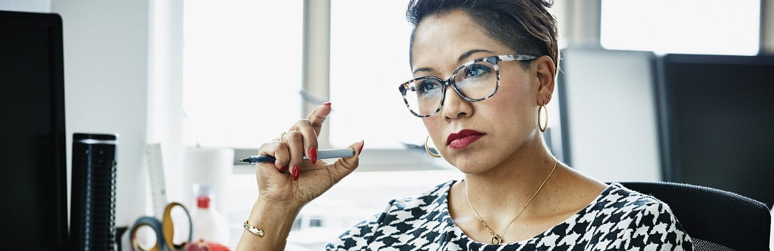 Woman sits at a desk holding a pen.